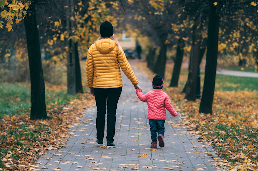 A parent walks hand-in-hand with a young child along an outdoor path, reflecting the parental bond at the center of child custody and relocation decisions.
