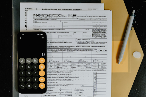 A calculator, pen, and tax documents on a desk beside a set of house keys — a divorce attorney helps clients understand the tax consequences of a settlement before signing.